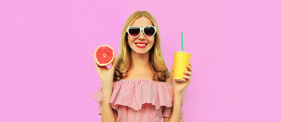 Summer portrait of happy smiling young woman drinking fresh juice with slice of juicy grapefruit wearing heart shaped sunglasses on pink background