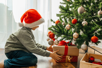 A boy, a child takes out a Christmas present from under the New Year tree, a box with a red ribbon....