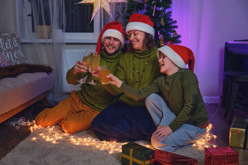 Happy family drinks non-alcoholic juices from a glass at the Christmas tree in the night light of a...