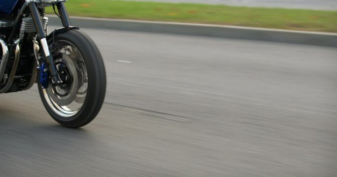 Close-up of a motorcycle riding on a road at high speed. Side view. Driving Bike on Streets. Speed Motion in Cityscape. Fast TRACKING Shot of a biker riding his custom built cafe racer through city.
