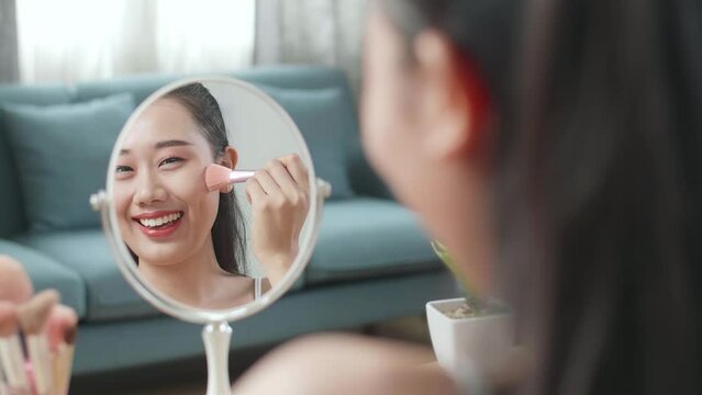Reflection In A Mirror Beautiful Young Asian Woman Rouging Her Cheeks And Smiling While Applying Makeup At Home

