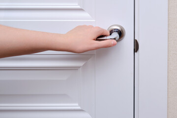 A woman opens the door holding the handle, hand close-up. White wooden door, metal door handle and...