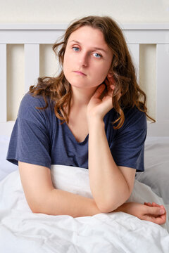 Portrait Of An Adult Woman Sitting On A Bed With A Blanket In A White Bedroom. A Brunette Woman Touches Her Hair And Looks At The Camera, 35 Year Old Female