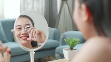 Reflection In A Mirror Beautiful Young Asian Woman Using An Eyelashes Curler And Smiling While Applying Makeup At Home
