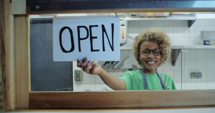 Happy African American woman looking at camera in a store or restaurant with an open sign.