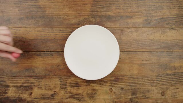 Vue de dessus d'une main de femme qui prend le dernier bonbon fraise dans une assiette blanche et le remet