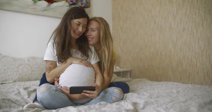Pregnant multinational lesbian couple look at an ultrasound image of his baby on the phone. LGBT