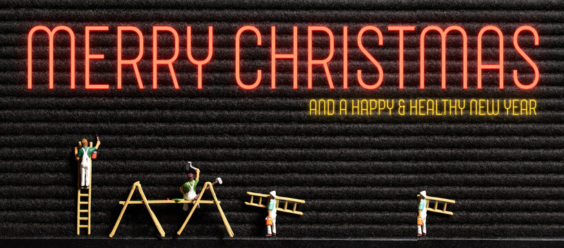 neon message MERRY CHRISTMAS AND A HAPPY AND HEALTHY NEW YEAR on a letter board with tiny painter figures