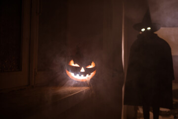 Halloween concept. Creepy silhouette in the dark corridor with pumpkin head. Toned light with fog on background.