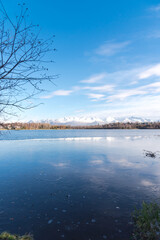 Freezing icy water on Westchester Lagoon with reflection of Chugach Mountains and fall landscape during October in Anchorage, Alaska