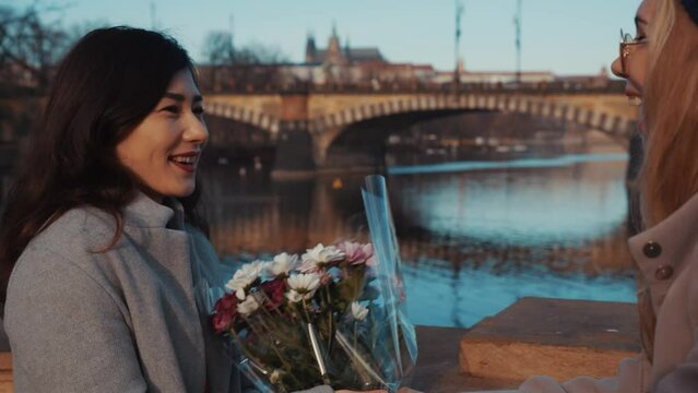 Close-up portrait of happy lesbians on date. Blonde girl giving asian girlfriend bunch of flowers. Young homosexual couple spending time together on holiday of valentine day. Romantic, LGBTQ concept