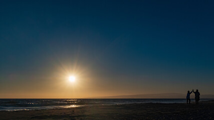 Fototapeta na wymiar Sunset on quiet beach showing couple playing on sand