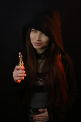 portrait of a beautiful young red-haired girl on a dark black background in the studio, with a cleavage and big breasts in black hoodie lets out smoke, smokes