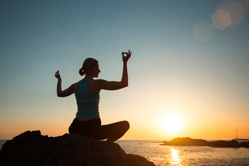 Silhouette of yoga woman, meditating on the ocean beach during a beautiful sunset.