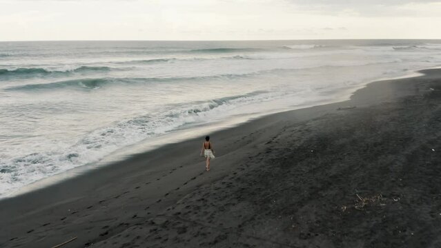Woman Walking On The Black Sand Beach Of El Paredon In Guatemala - aerial drone shot