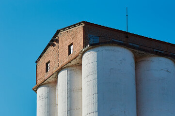 A fragment of the roof of the granary of the agro-industrial complex against the blue sky. White containers for grain