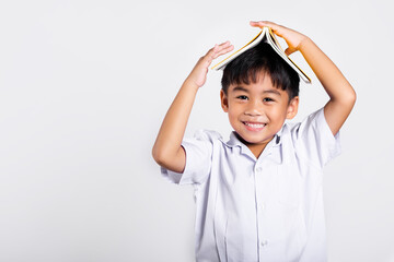 Asian adorable toddler smiling happy wearing student thai uniform red pants stand holding book over...