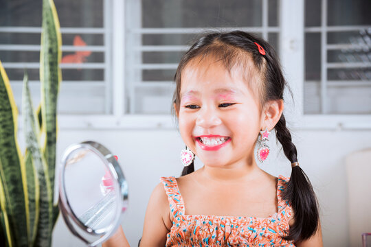 Asian adorable funny little girl making makeup her face she look in the mirror and applying red lipstick to mouth, Learning activity to be woman, happy kid is beautiful make up with cosmetics toy
