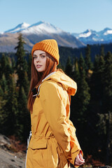 Woman in yellow raincoat hiking stands in front of mountains in yellow cap autumn sunset light 