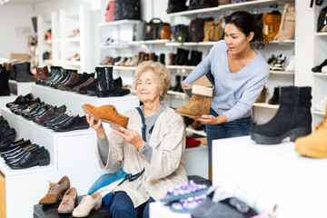 Friendly female sales consultant working in a shoe store serves a mature woman who is going to try...