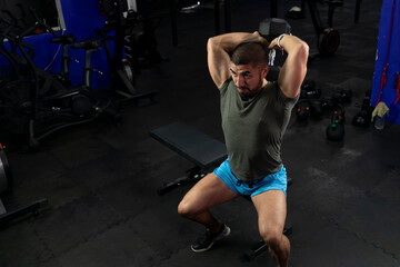 Fototapeta na wymiar Muscular Latino man doing exercises for biceps sitting on a gym bench