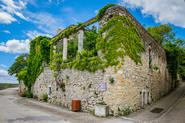 The beautiful and green narrow streets of the medieval village of Lussan, with old stone house and...