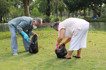 volunteer tourist asian senior couple cleaning up garbage and plastic debris on dirty park by collecting them into big black bag