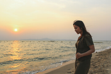 A young woman wearing a green dress stands in the sea at the beach enjoying the early summer morning sunrise view.