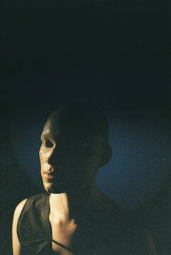 Vertical image of woman with shaved head standing in dark with her eyes closed