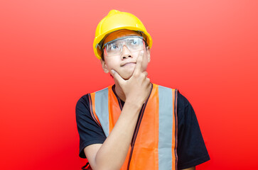 young asian man construction worker using yellow helmet and orange vest makes thinking gesture....