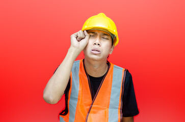 young asian male construction worker using yellow helmet and orange vest crying. asian male worker in crying and sad with gesture wiping tears.