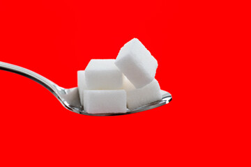 Sugar cubes in a spoon on red background