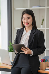 The image pretty smiling Asian businesswoman standing holding a tablet. Looking at the camera.