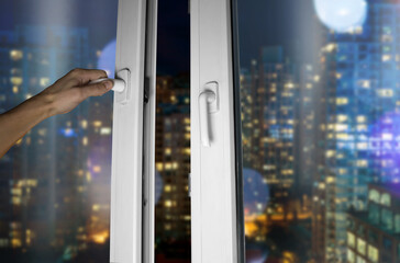 Hand opens the window with a view of the night city
