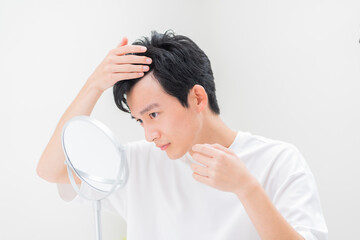 鏡を見て髪の毛を気にする若い日本人男性