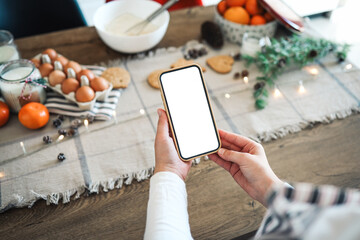 Phone with a blank screen in the hands on the background of Christmas cooking. Place for text. Master class invitation. Merry Christmas