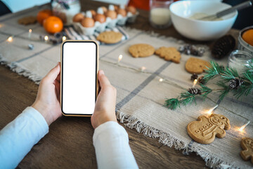 Phone with a blank screen in the hands on the background of Christmas cooking. Place for text. Master class invitation. Merry Christmas