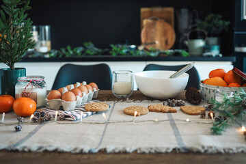 Ingredients for making Christmas cookies on the table against the backdrop of the kitchen. Plate with dough, milk, egg and New Year's decor