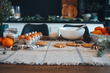 Ingredients for making Christmas cookies on the table against the backdrop of the kitchen. Plate with dough, milk, egg and New Year's decor