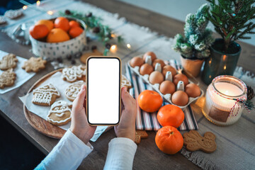 Phone with a blank screen in the hands on the background of Christmas cooking. Place for text. Master class invitation. Merry Christmas