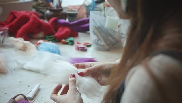 Woman creates doll angel smoothing piece of wool for wings