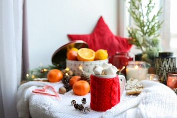 Fototapeta na wymiar A cup of cocoa with marshmallows in a red knitted decoration in a New Year's interior