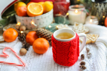 Obraz na płótnie Canvas A cup of tea with a knitted red decoration, tangerines, candles, a garland. Christmas atmosphere in the house
