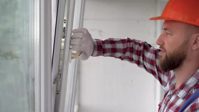Male worker in overalls installing window in flat. Professional handyman close and fixing window at home.