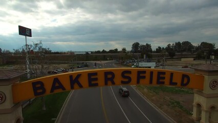 Aerial Backward Shot Of Entrance Overhead Sign Board Over Road In City Under Cloudy Sky - Bakersfield, California