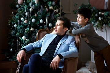 A young dad and his son in festive attire are in a room decorated for the New year and Christmas. *