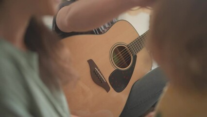 Happy young multiethnic parents and their toddler son spend time together and play guitar at home. Woman, man and a kid sitting on sofa and smiling. Music family and creativity concept. Couple in love
