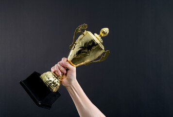 Human hand holding golden trophy cup on black background