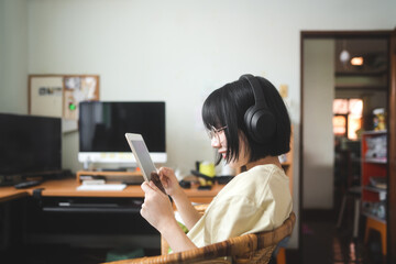 Young adult asian woman wear headphone listen music and relax using digital tablet for internet