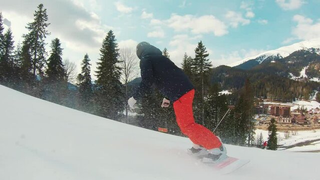 Side view in motion person on snowboard descends from snowy mountain with speed. Outdoors beautiful nature landscape with trees and mountains. Leisure activity in sport lifestyle. Panning slider.
